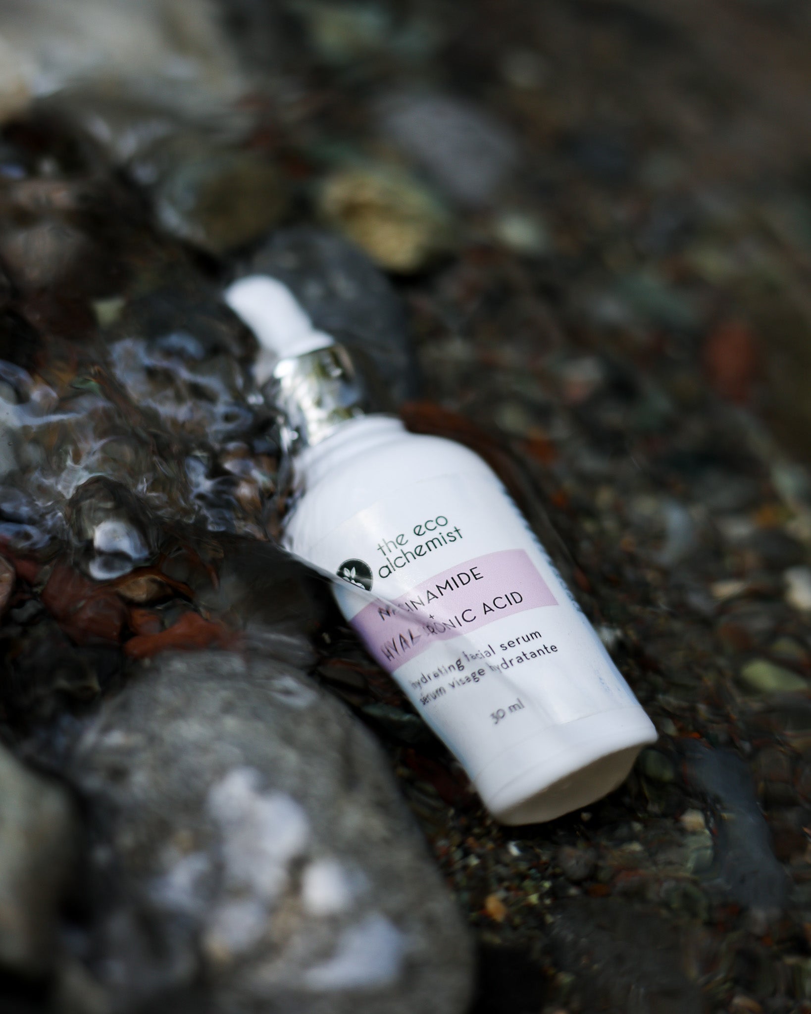 Niacinamide + Hyaluronic Acid Hydrating Facial Serum in water surrounded by rocks